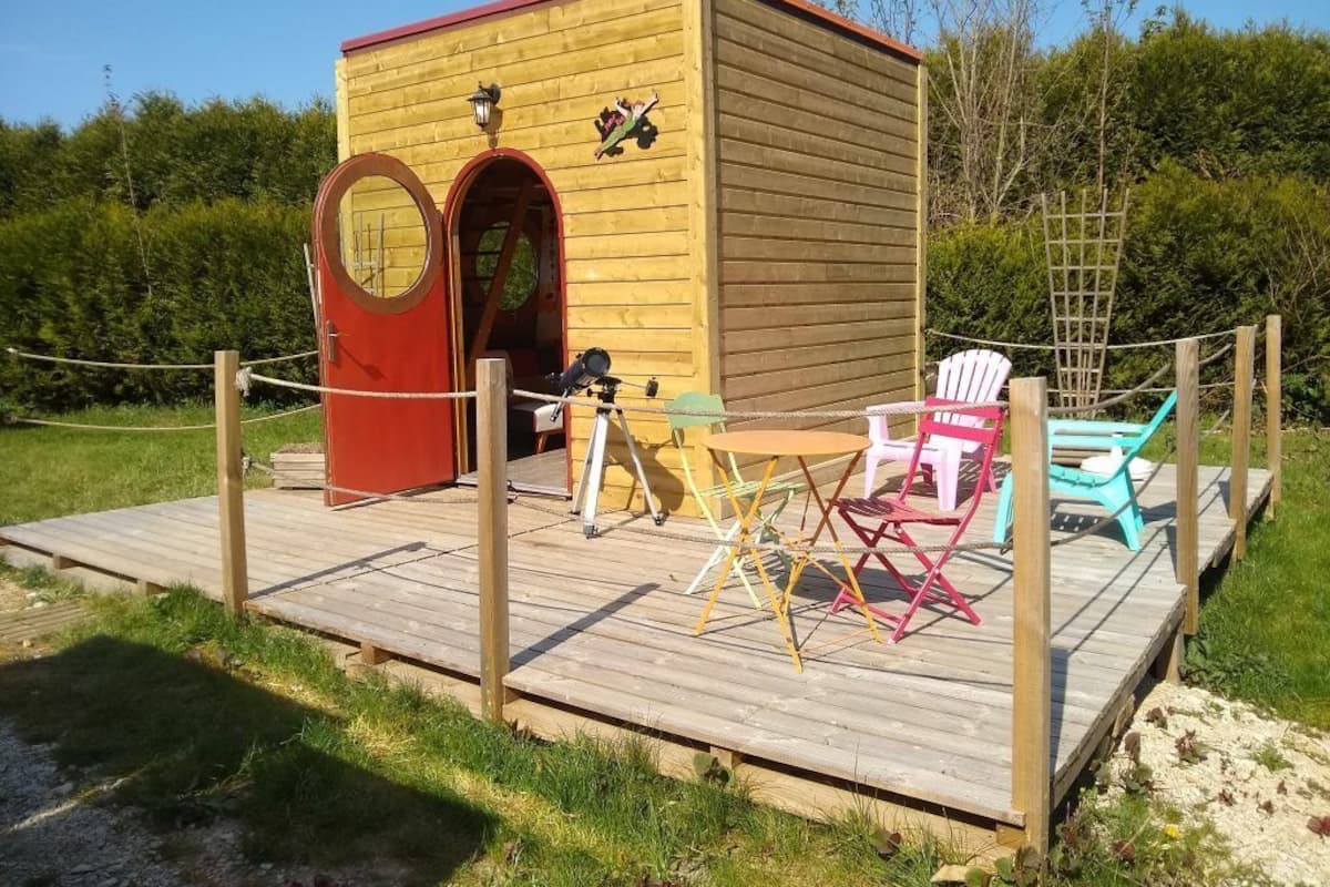 A wooden cabin with a red door and a small table with chairs on a wooden deck.