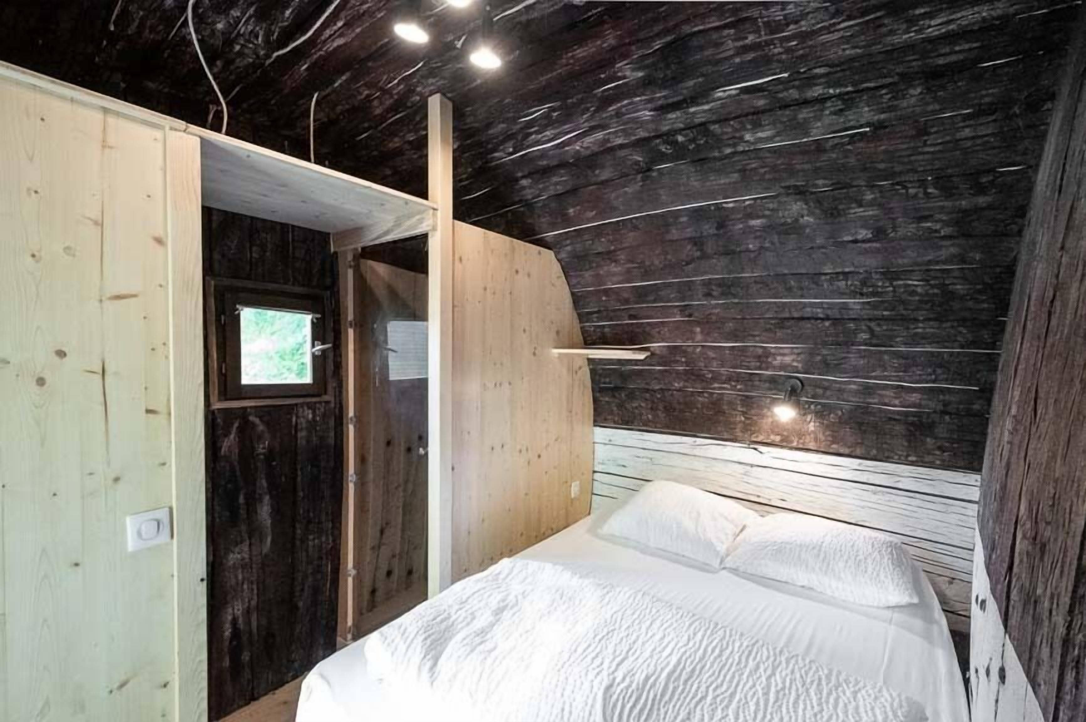 A bedroom with a wooden ceiling, a bed, and a small window.