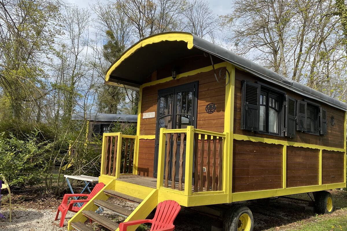 A wooden cabin with a yellow exterior, a covered porch, and a small deck with red chairs.