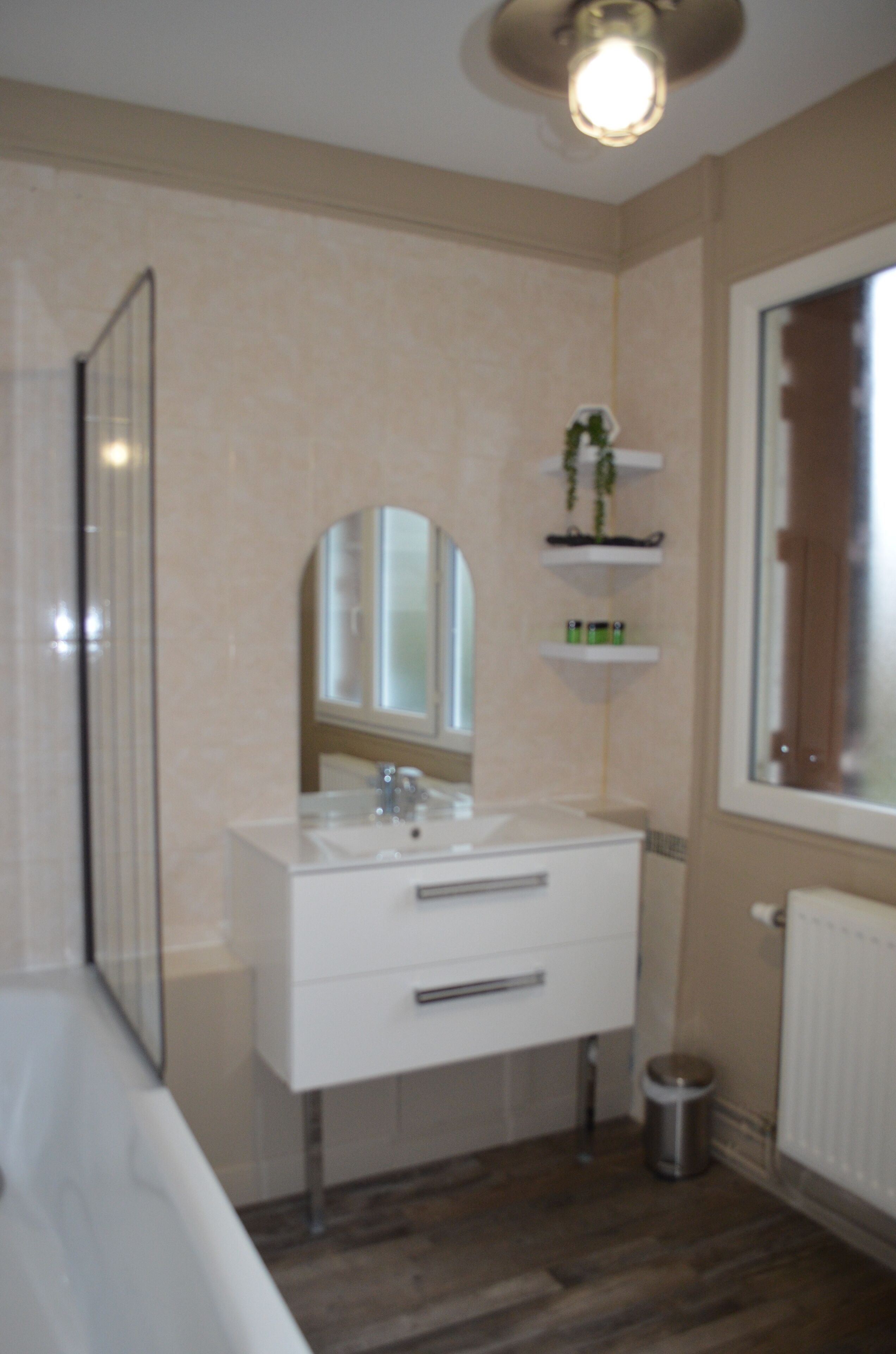 Een badkamer met een witte wastafel, een spiegel, een wasbak, een toilet, een prullenbak en een raam met uitzicht op het buiten.