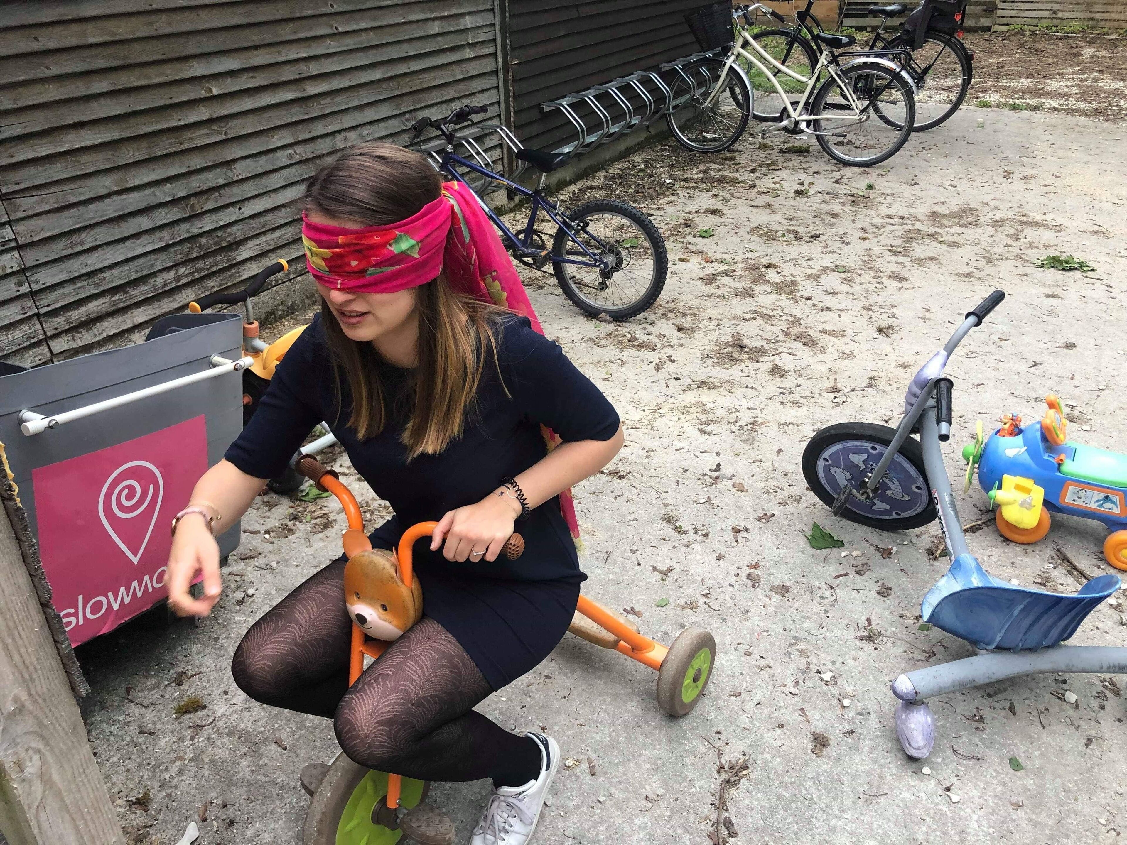 Una persona montando un triciclo con una cesta, estacionado sobre una superficie de concreto con bicicletas al fondo.