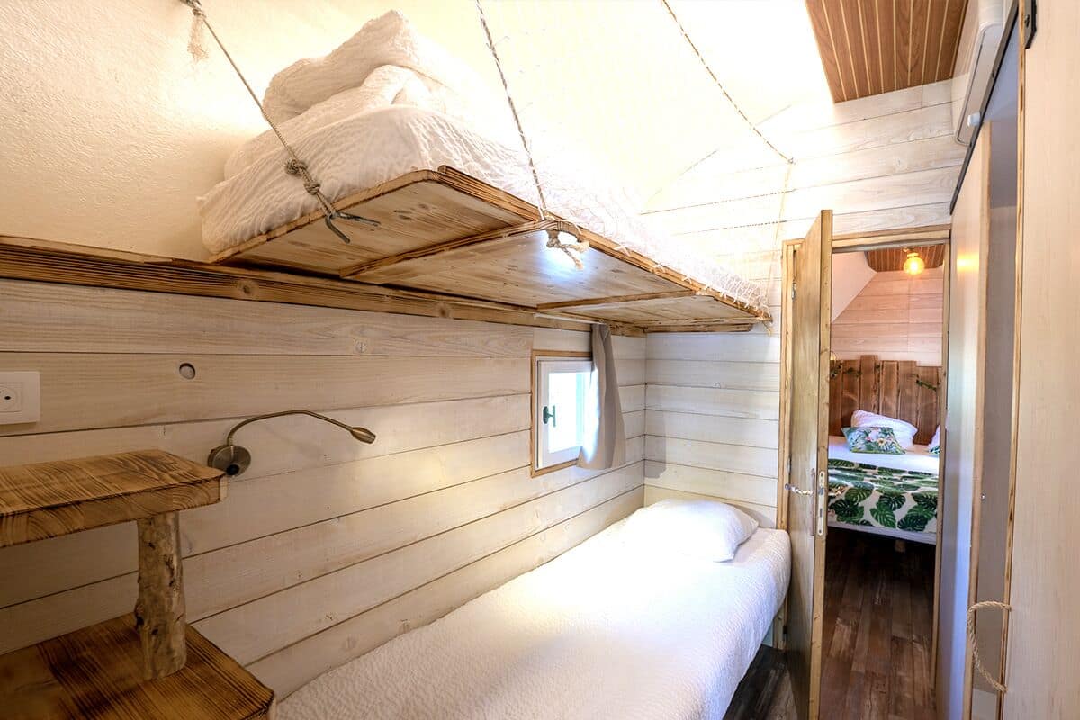 A small, cozy room with a bunk bed, a wooden shelf, and a small window.