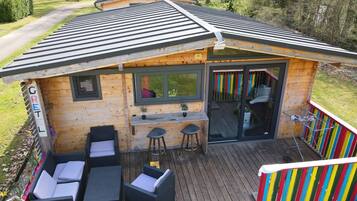 A wooden cabin with a deck, outdoor seating, a bar area, and a sliding glass door.