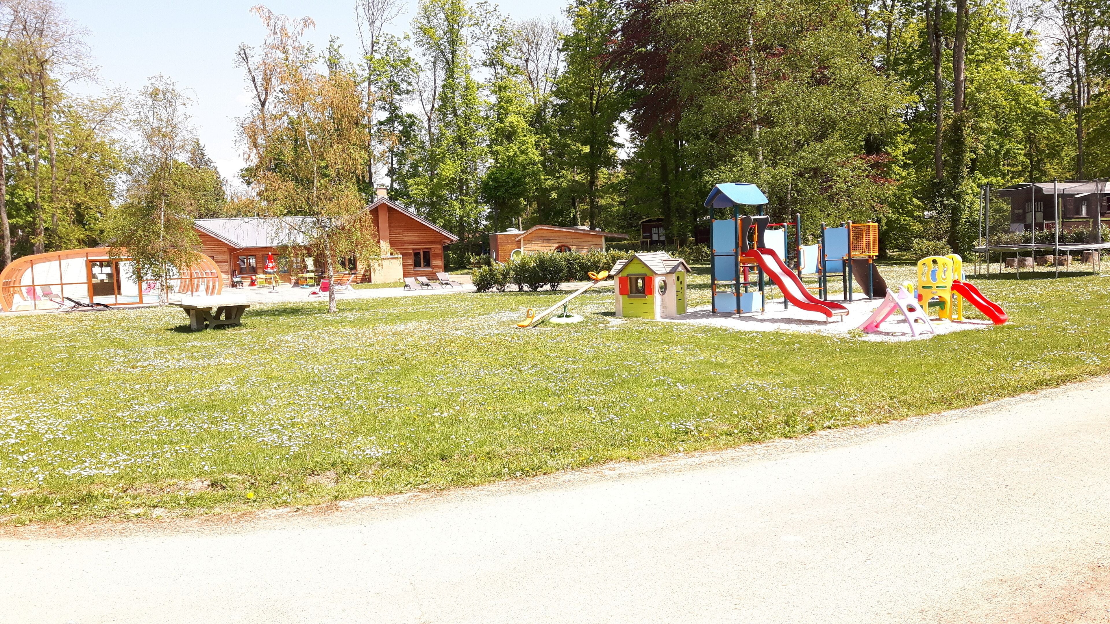 A playground with various play structures, a small wooden building, and a covered seating area.