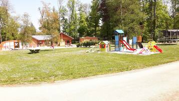 A playground with various play structures, a small wooden building, and a covered seating area.