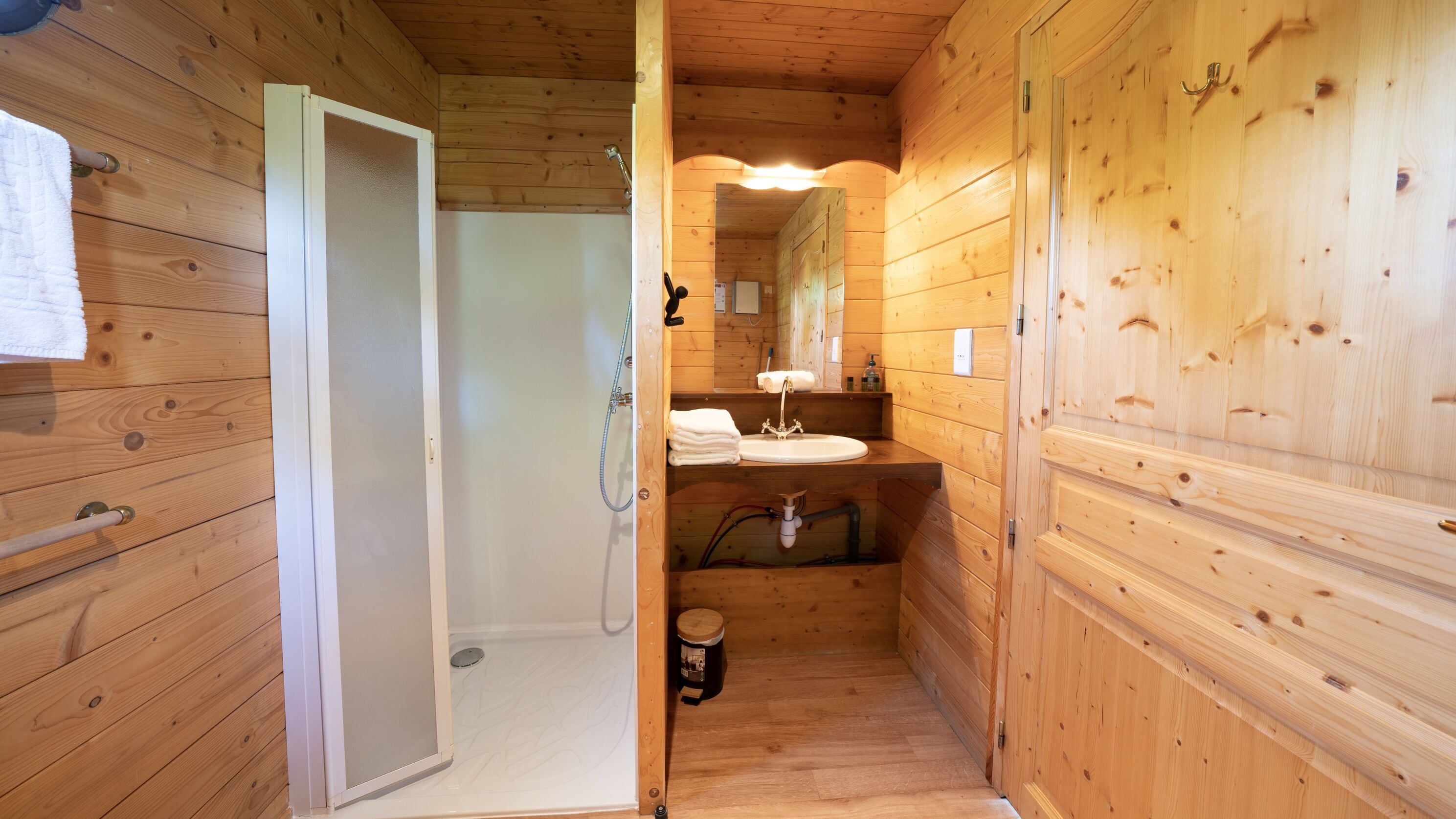 Une salle de bain rustique, aménagée dans une cabane en bois, avec une douche, un lavabo et des toilettes.