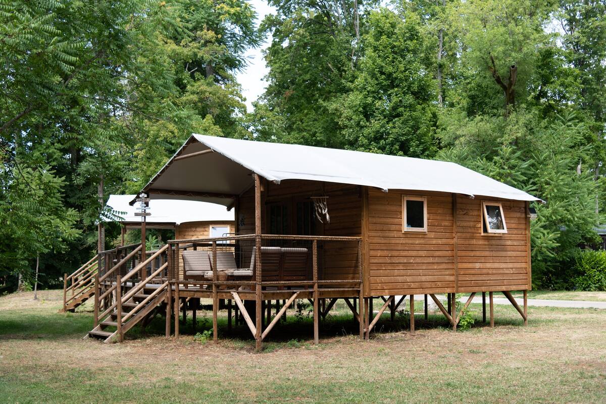 A wooden cabin with a porch and stairs, surrounded by trees.
