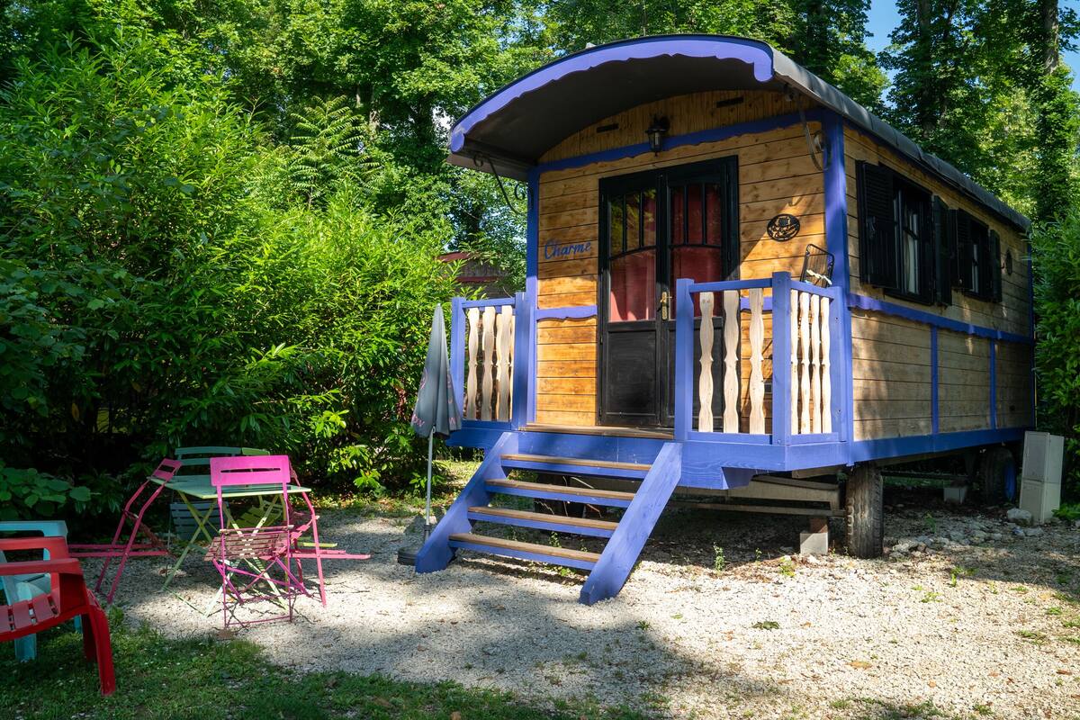 A wooden cabin with a porch and steps, surrounded by greenery.