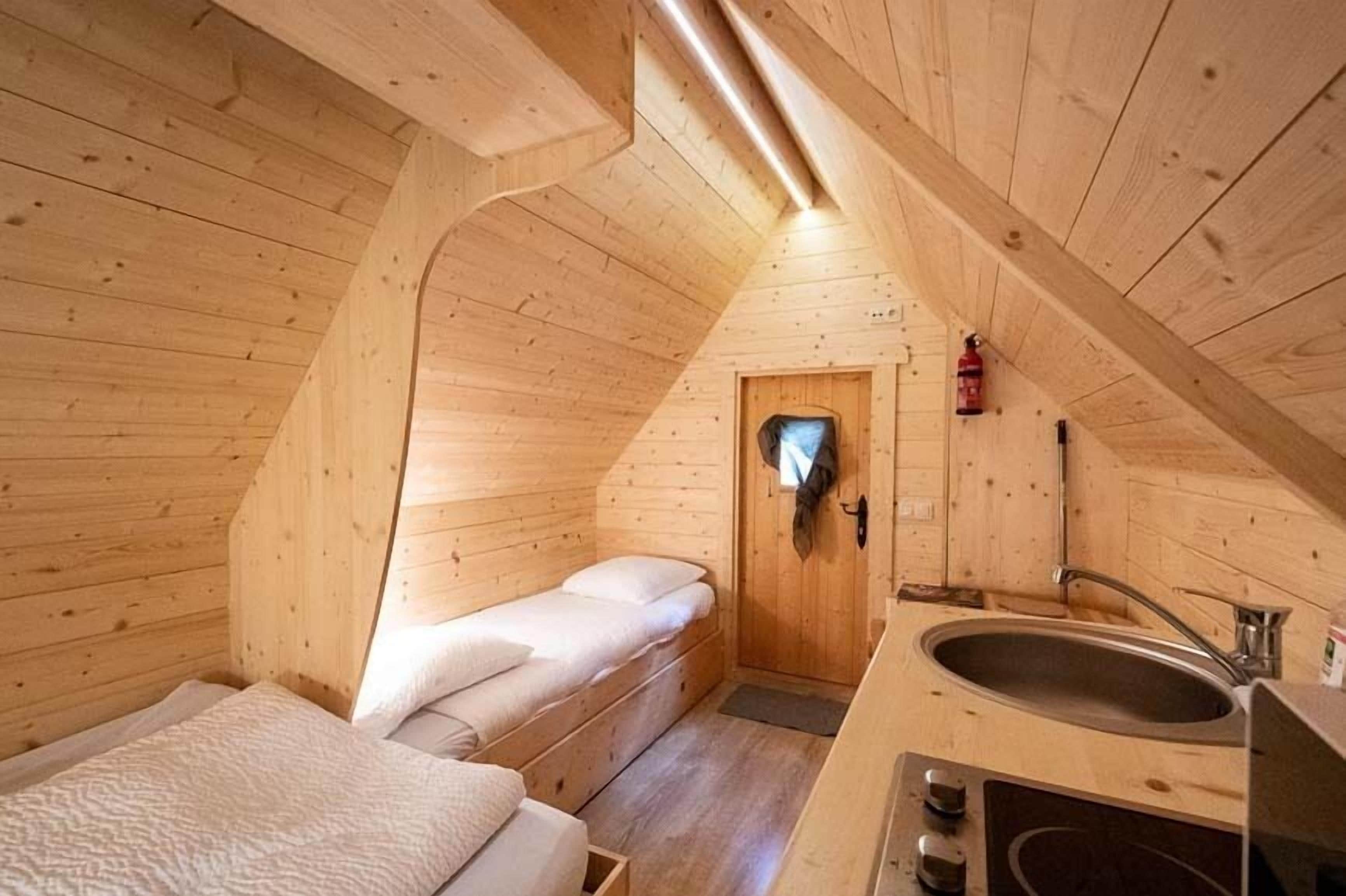 Une petite cabane en bois avec un lit simple, un lavabo et une porte donnant sur une salle de bain.