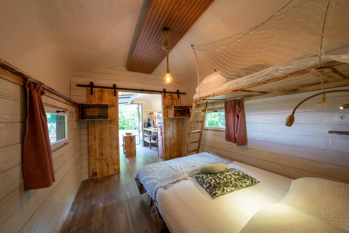 A wooden cabin with a bed, a desk, and a window.