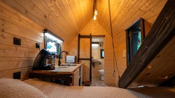 Interior acogedor de una cabaña con paredes de madera, una kitchenette, un baño y un amplio ventanal.