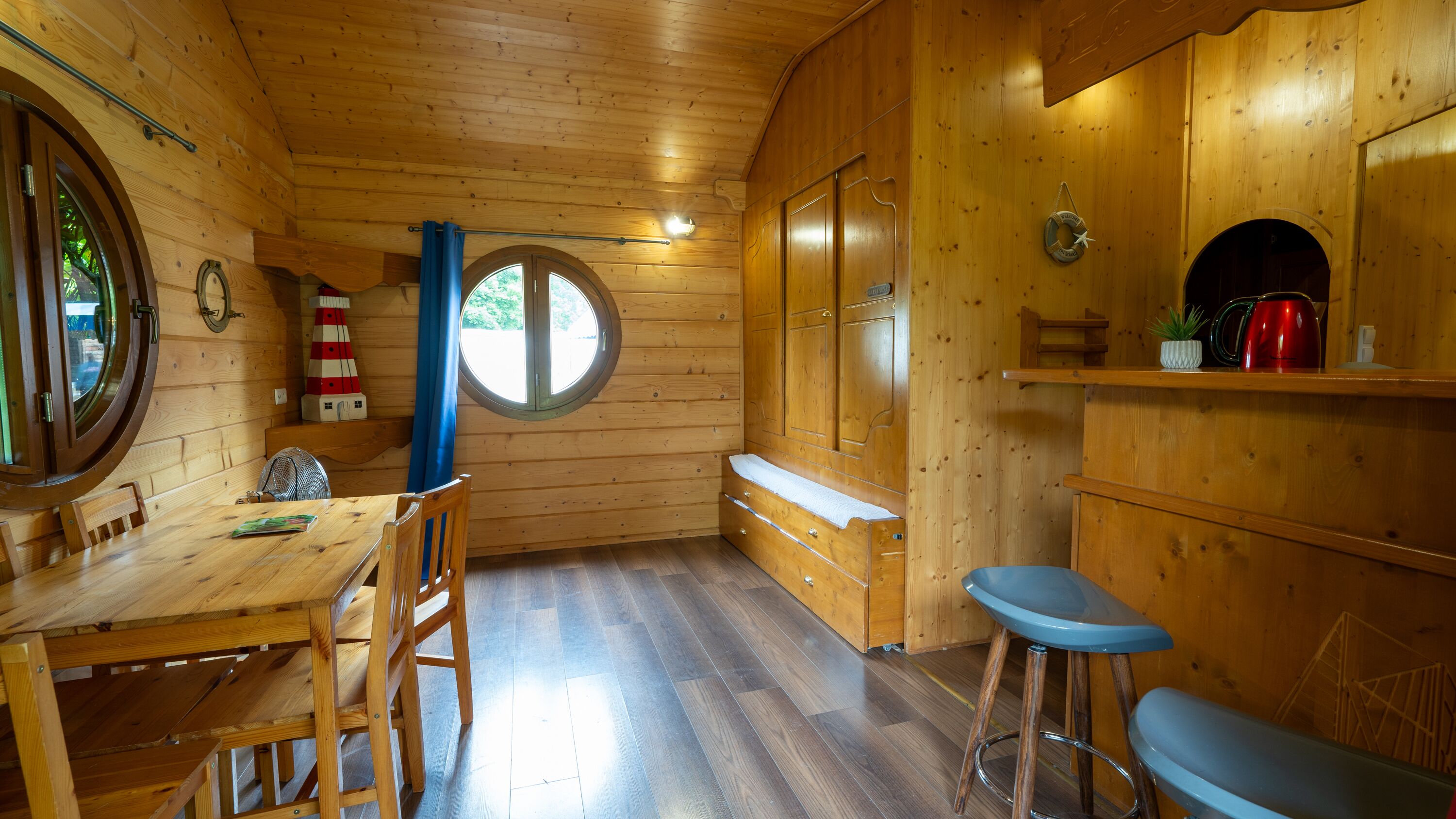 L’intérieur d’un chalet en bois comprend une table à manger, des chaises, un coin bar et une fenêtre circulaire.