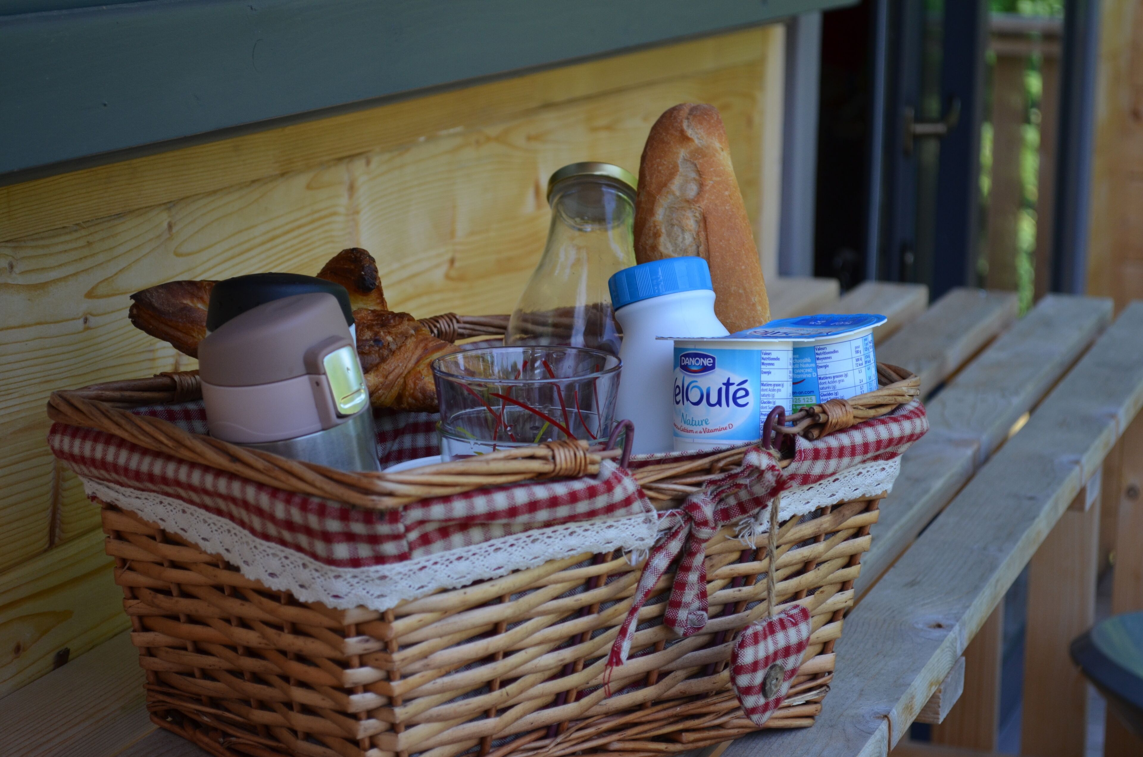 A wicker basket with food items and a bottle on a wooden bench.