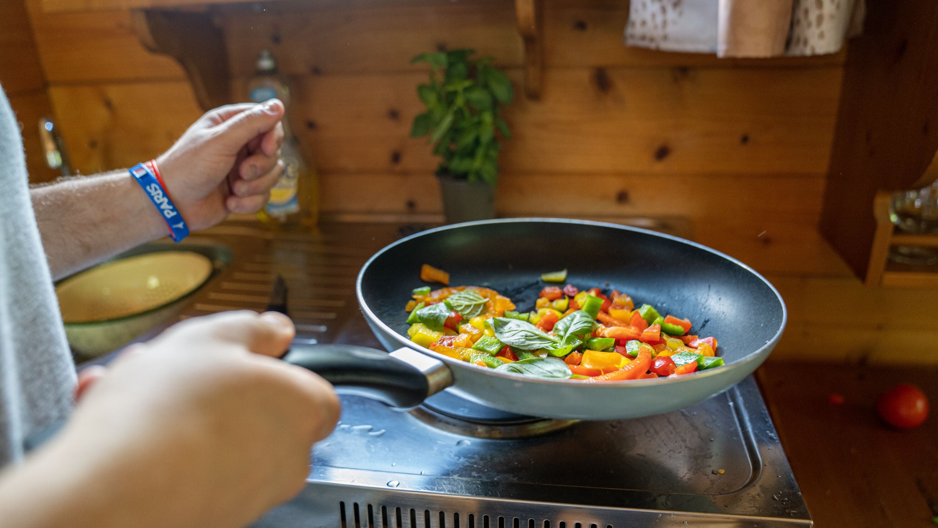 Une personne prépare un plat de légumes sautés et colorés dans une poêle sur une cuisinière.