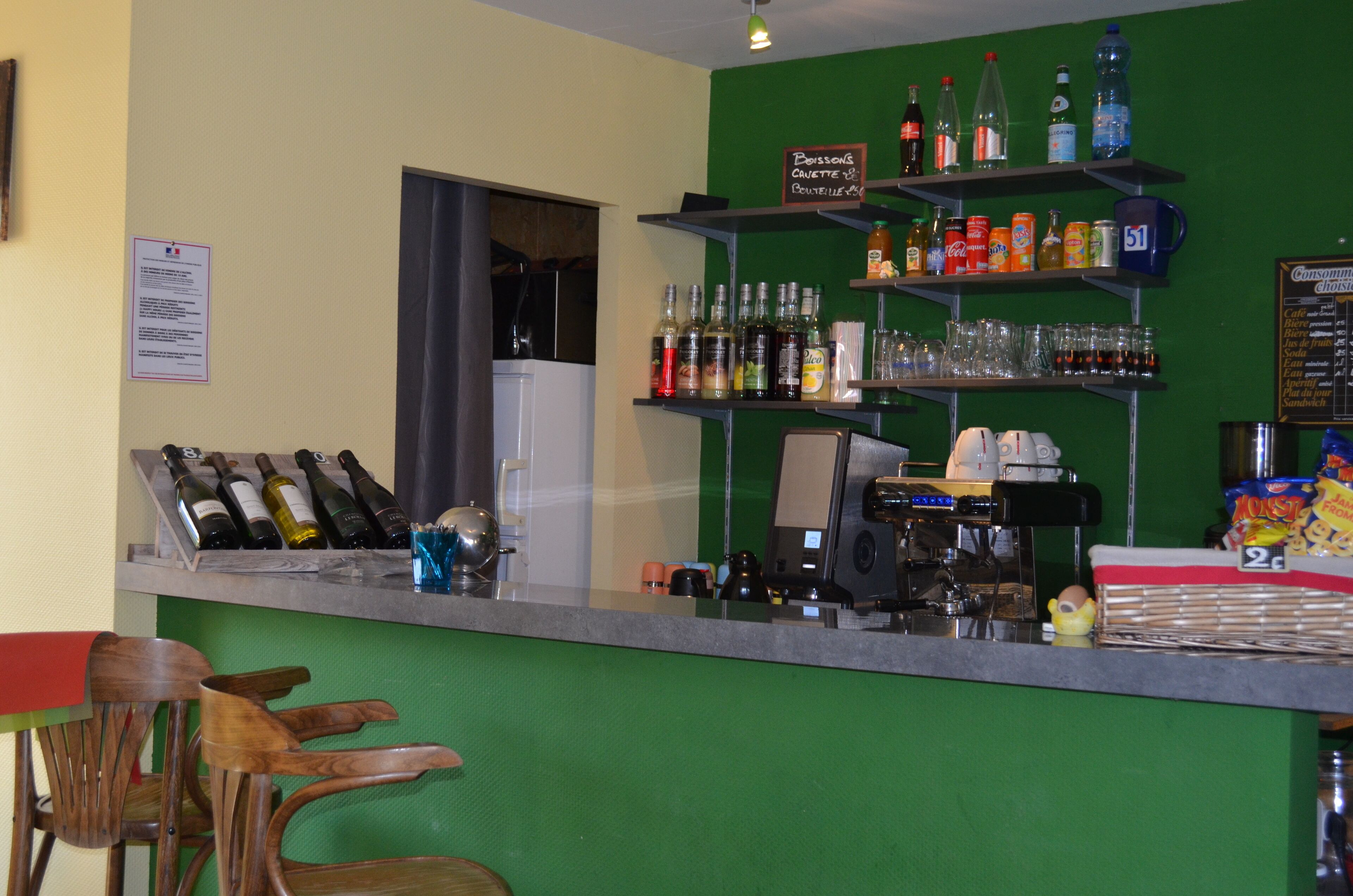 Een bar met flessen en glazen, een koffieapparaat en een zithoek met houten stoelen.