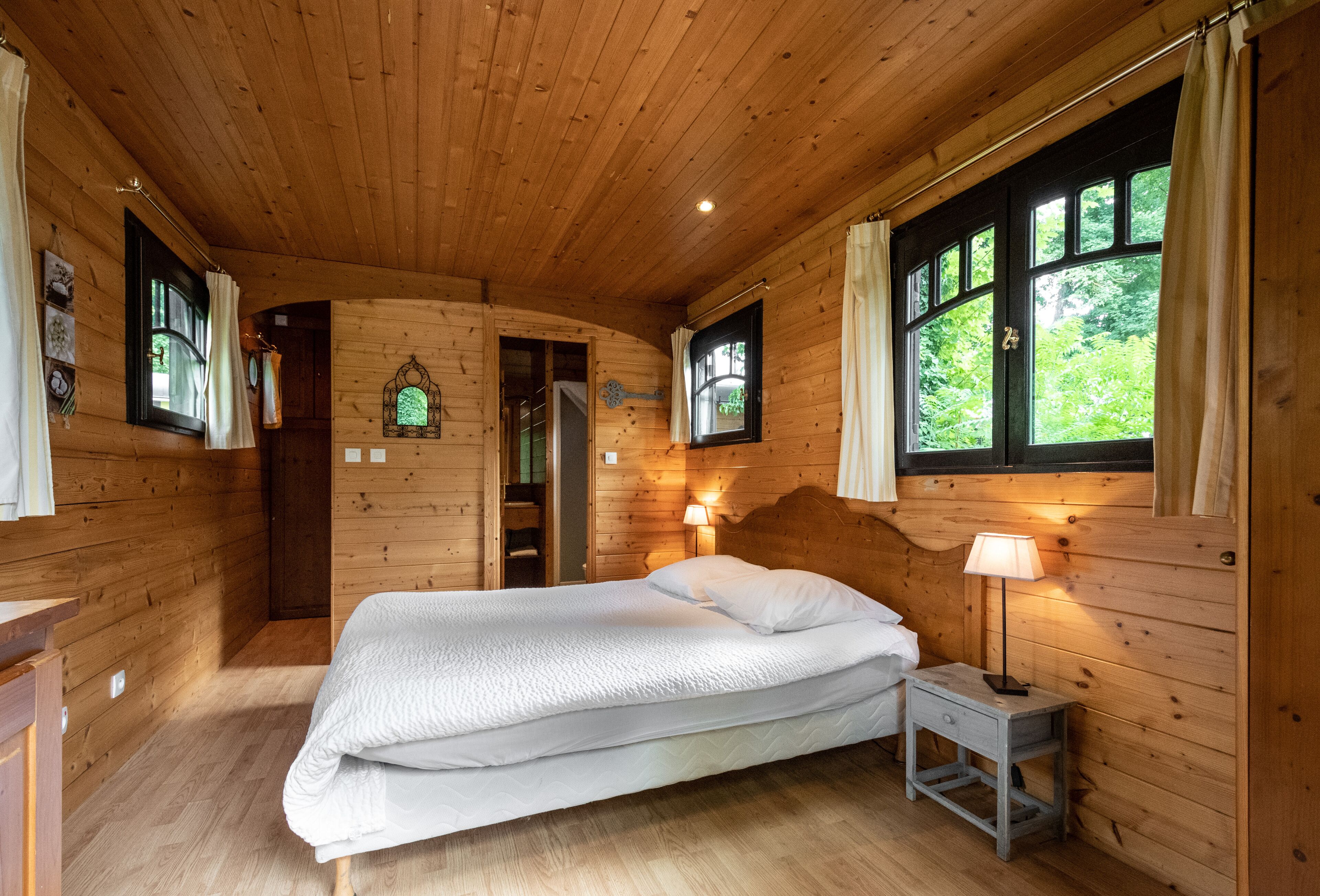 Un dormitorio de cabaña de madera con cama, mesita de noche y ventanas.