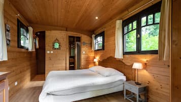 Un dormitorio de cabaña de madera con cama, mesita de noche y ventanas.