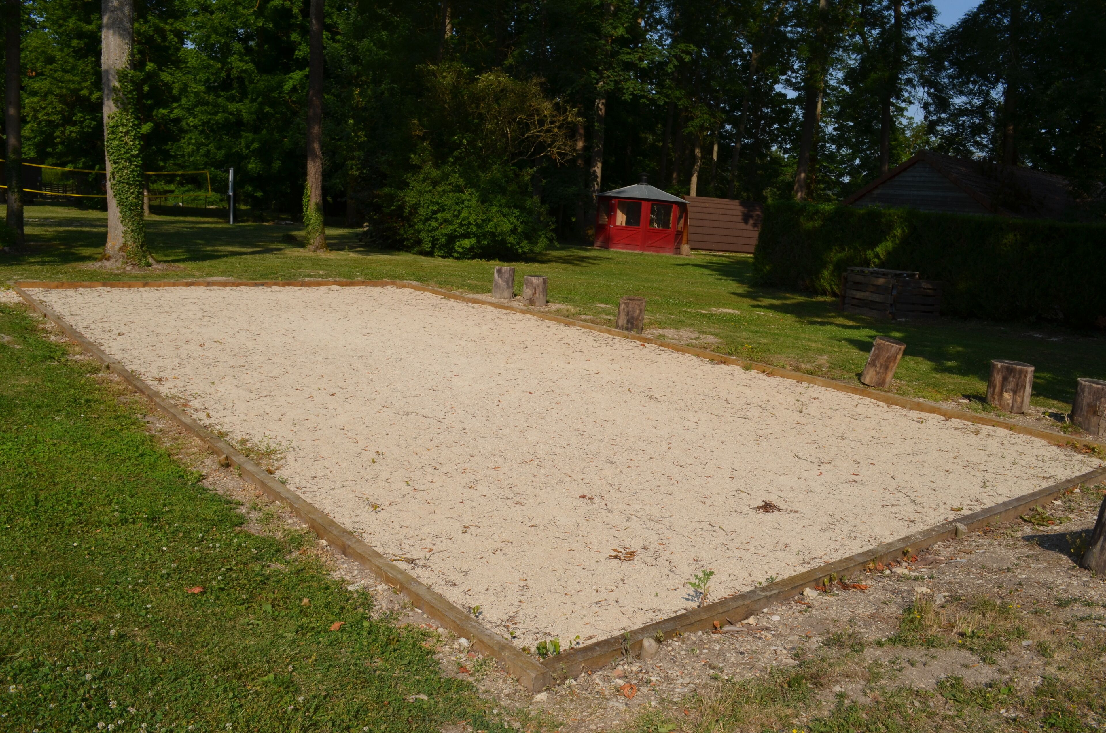 A sandy sports court with a wooden border, surrounded by grass and trees.