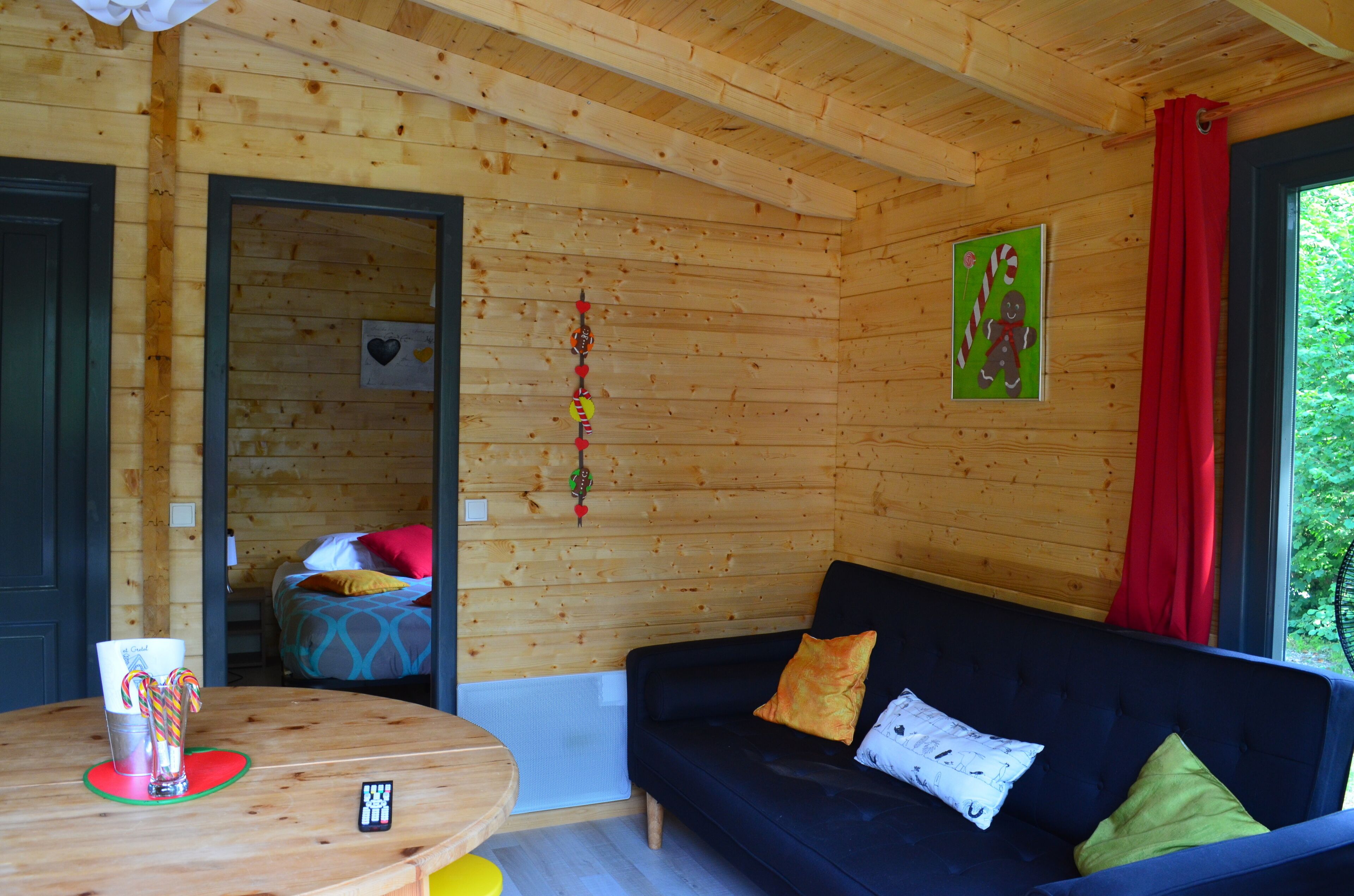 A cozy wooden cabin with a blue sofa, a wooden table with a remote control, and a door leading to a bedroom.
