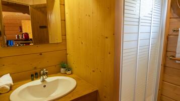 Une salle de bain rustique, aménagée dans une cabane en bois, avec un lavabo, un miroir et une douche.