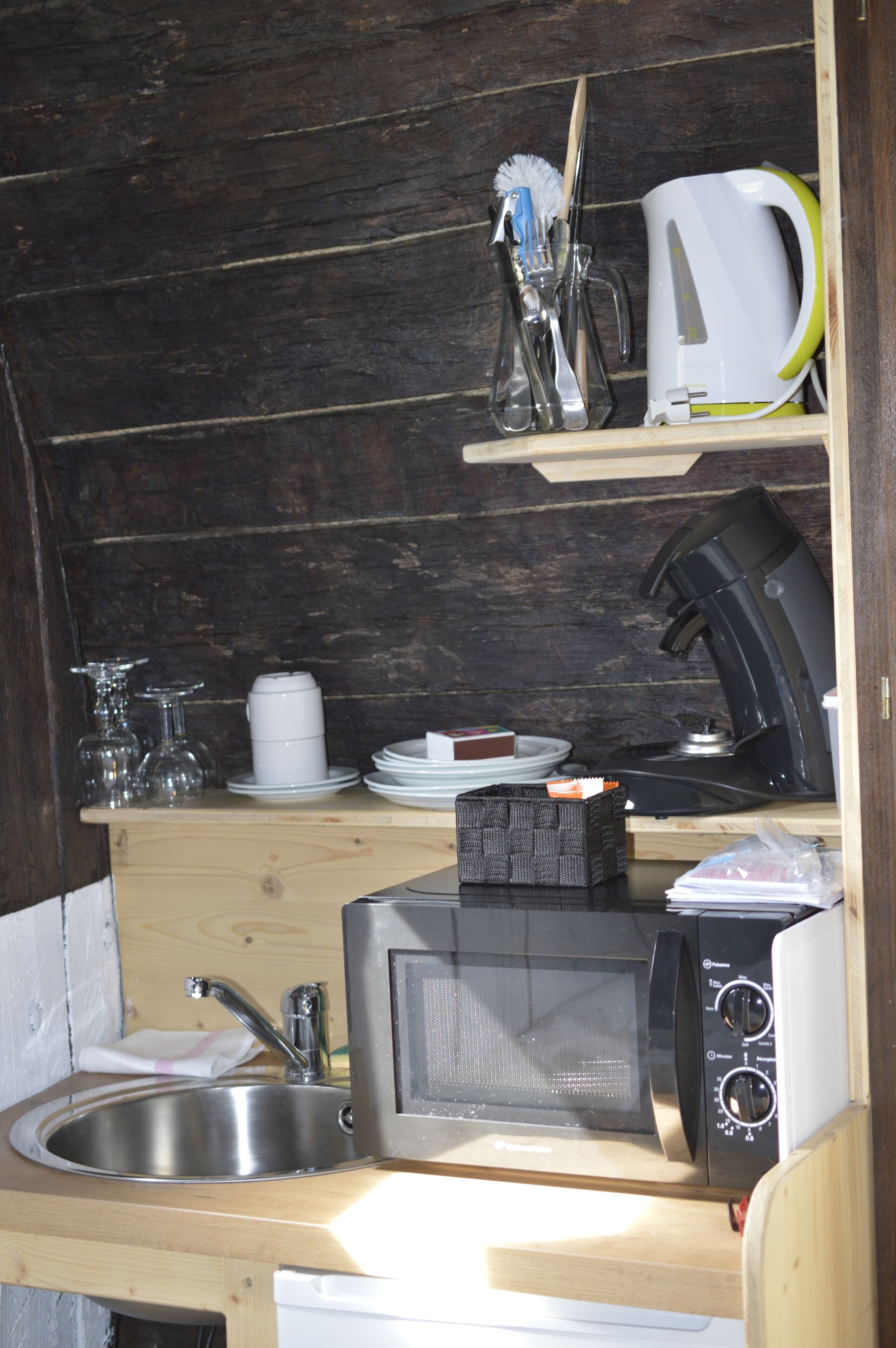 Une cuisine compacte équipée d’un évier, d’un four à micro-ondes et d’une machine à café, le tout installé sur un plan de travail en bois.