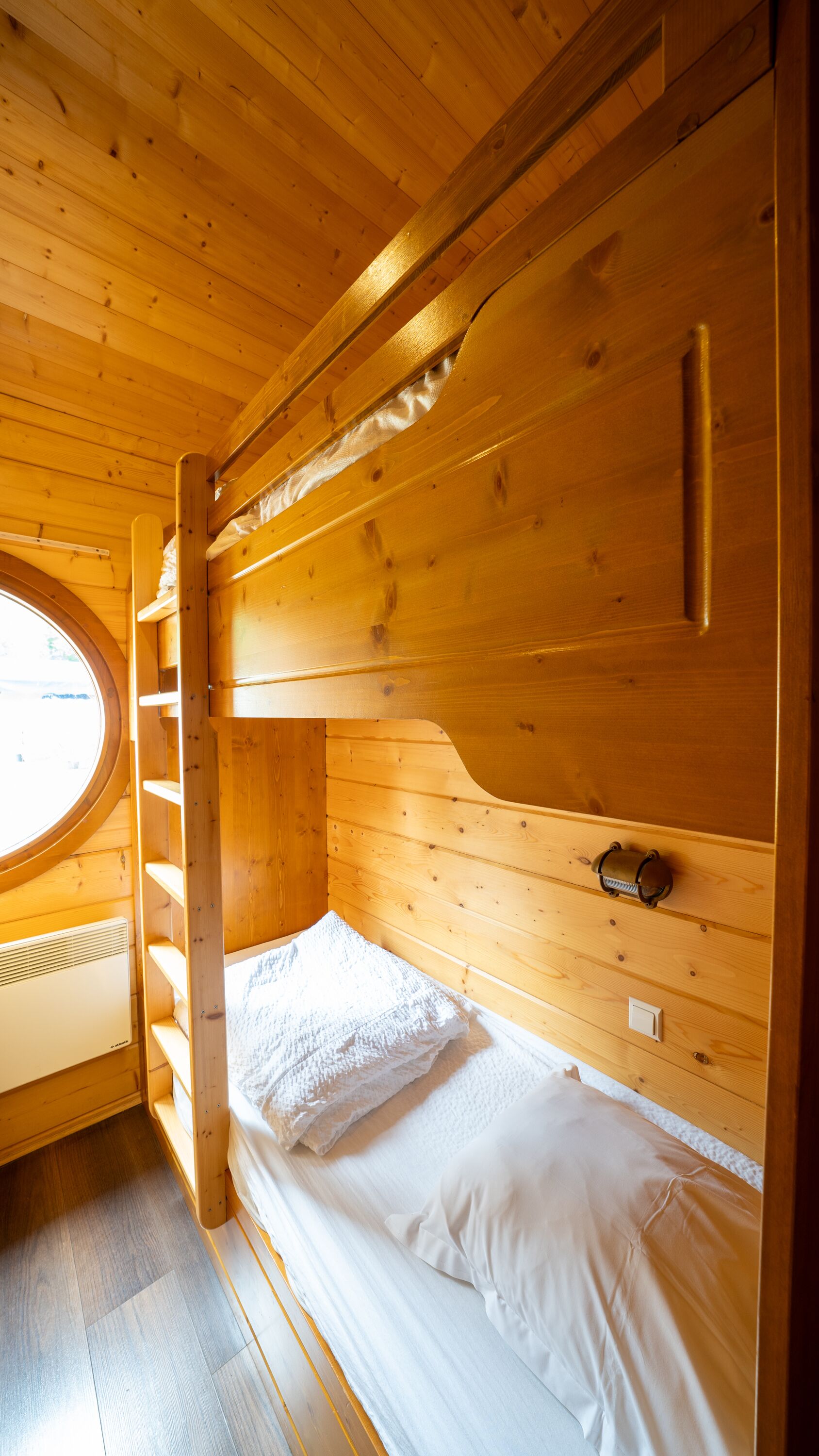 Habitación con literas de madera, tragaluz, calentador y un estante pequeño.