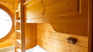 Habitación con literas de madera, tragaluz, calentador y un estante pequeño.
