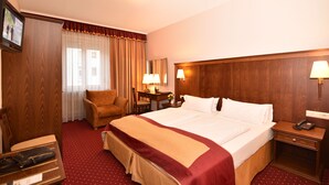 A hotel room with a large bed, a desk with a lamp, a chair, and a wooden wardrobe. - Hotel Römerhof (Baden-Baden)