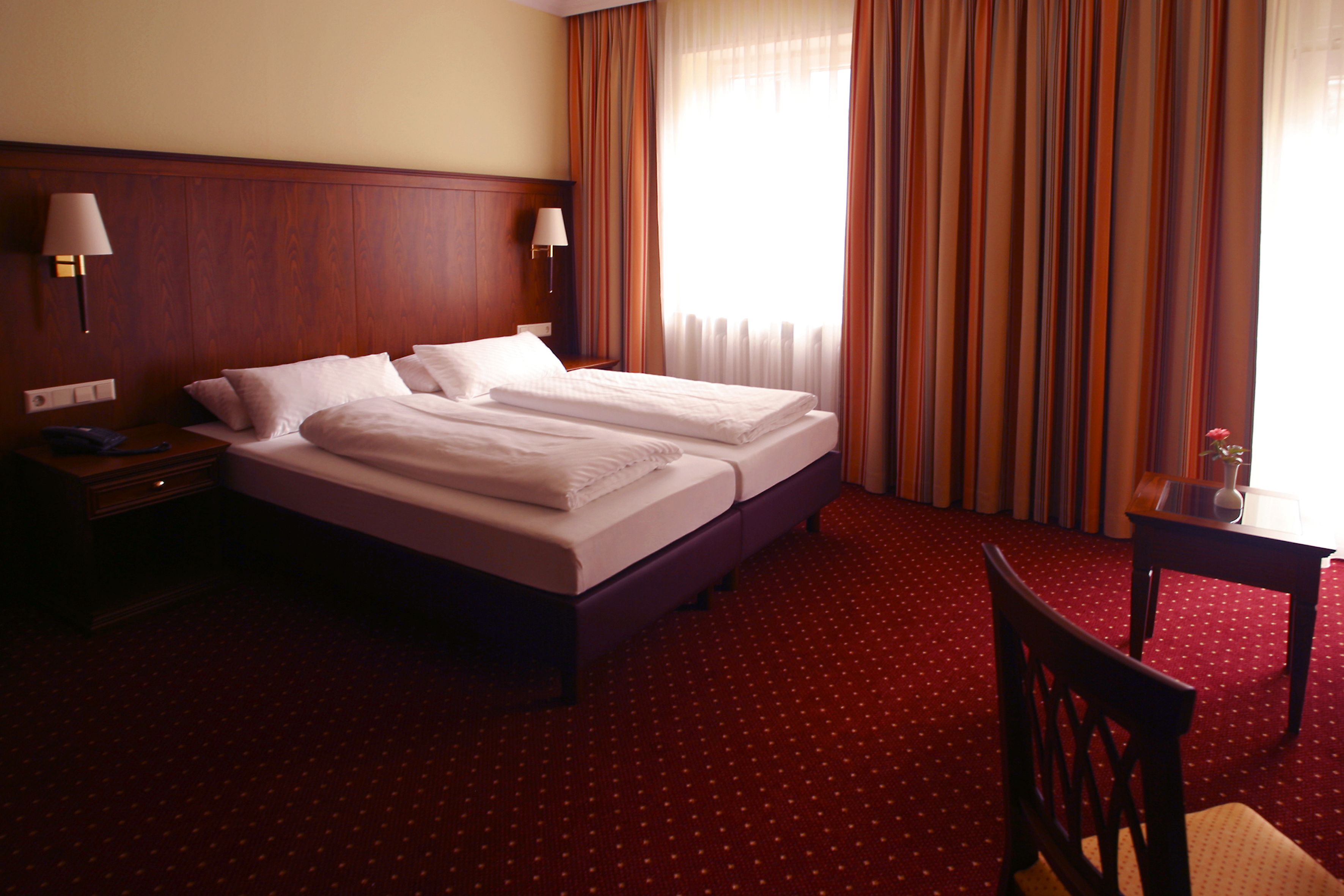 A hotel room with a large bed, two bedside tables with lamps, a small table with a vase, and a chair.