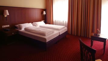 A hotel room with a large bed, two bedside tables with lamps, a small table with a vase, and a chair.