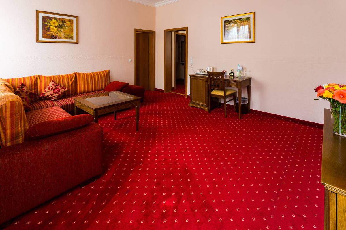 A room with a red carpet, a sofa, a wooden chair, a small table, and a vase with flowers.