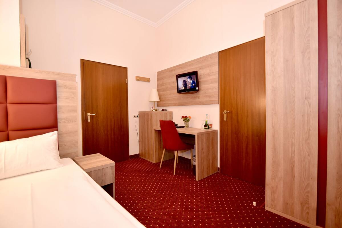 A hotel room with a bed, a desk, a chair, a TV mounted on the wall, and a wardrobe.