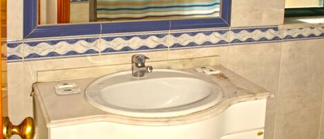 Un baño con lavamanos blanco, un espejo con marco azul y cortina de ducha a rayas.
