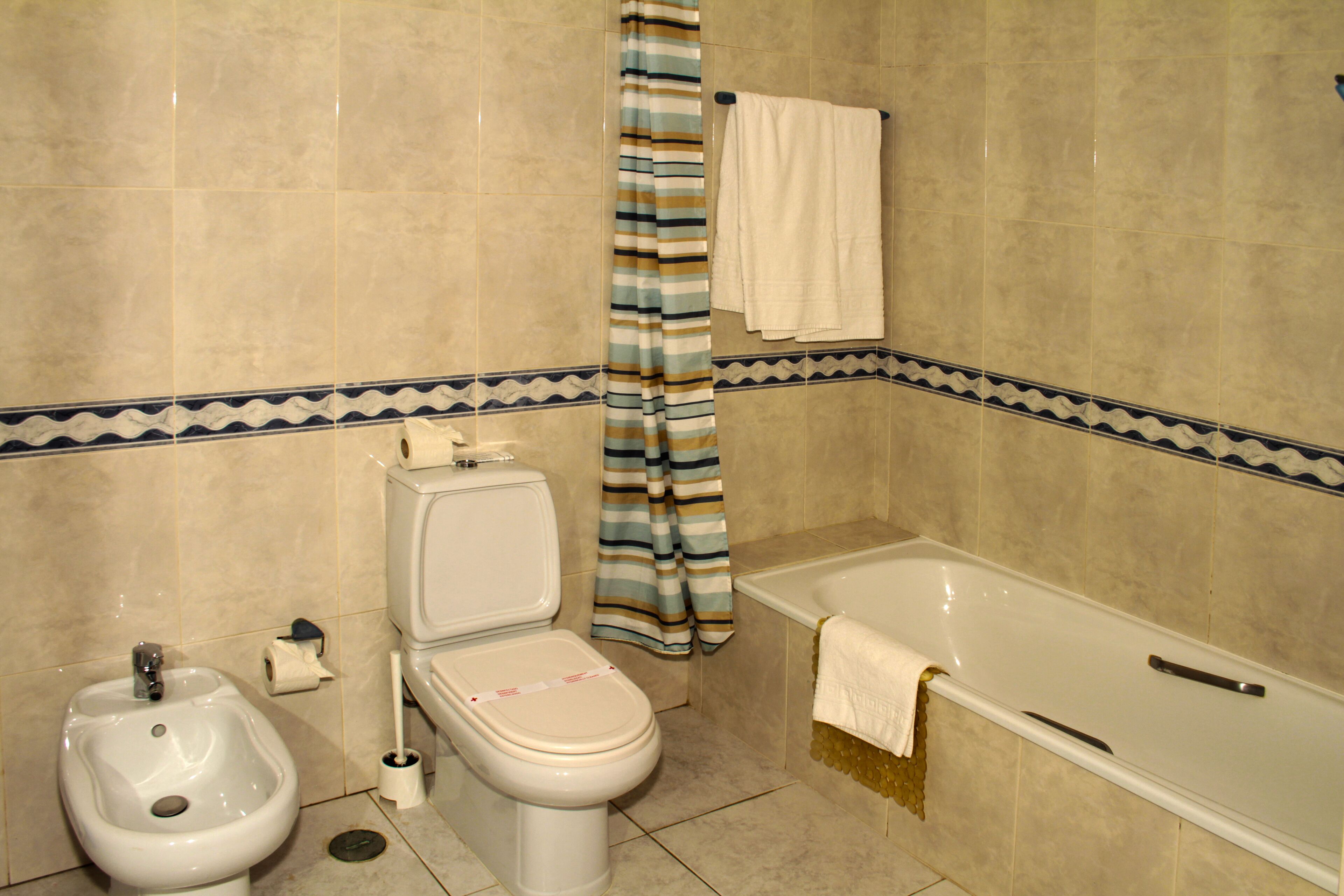 Une salle de bain équipée d’un bidet, de toilettes, d’une baignoire et d’un rideau de douche à rayures.