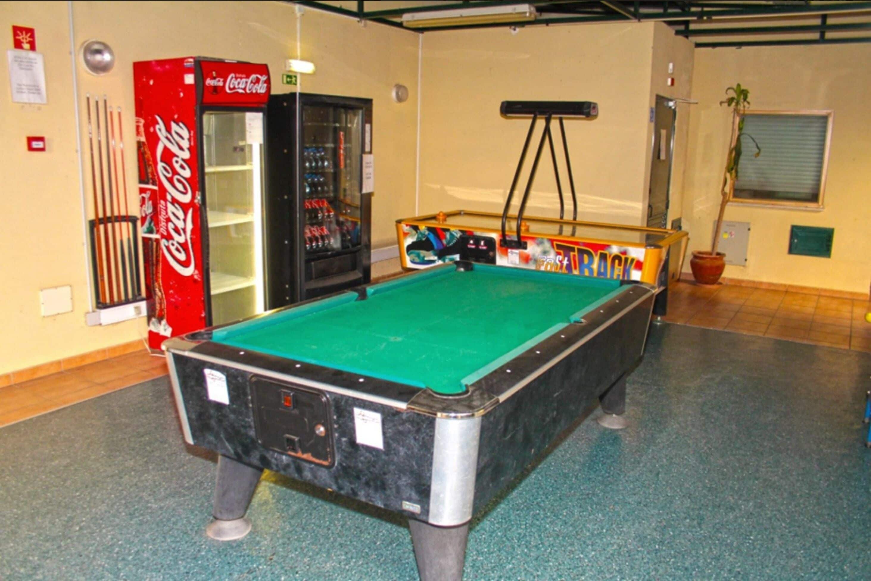 A pool table in a room with a Coca-Cola refrigerator and a vending machine.