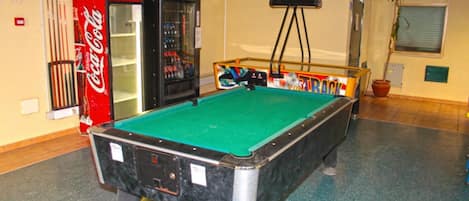 A pool table in a room with a Coca-Cola refrigerator and a vending machine.