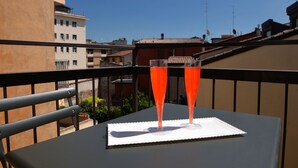 A balcony with two glasses of red beverage on a table, overlooking a cityscape. - Hotel Siena (Verona)