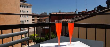 A balcony with two glasses of red beverage on a table, overlooking a cityscape.