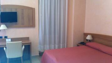 A hotel room with a bed, a desk, a chair, a television, and a window with curtains.