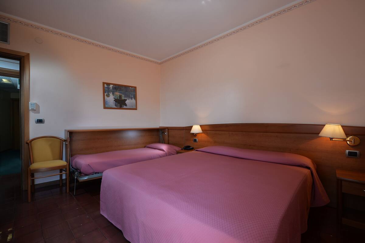A hotel room with two beds, a chair, a painting on the wall, and two bedside lamps.