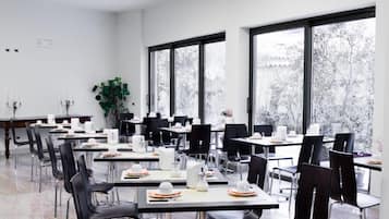 A modern dining area with tables and chairs, large windows, and a plant.