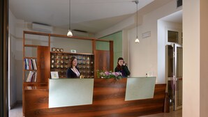 A reception desk with a wooden finish, a bookshelf with books, and a floral arrangement. - Hotel Siena (Verona)