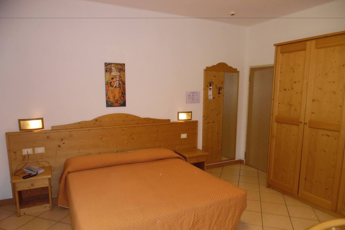 A bedroom with a wooden bed, a nightstand, a mirror, and a wardrobe.