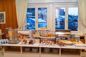 A buffet with various food items and a view of a snowy landscape through the windows.