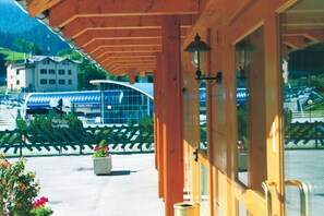A wooden building with a glass door and windows, a metal railing, and a view of a train in the background. - Hotel Andalo (Andalo)