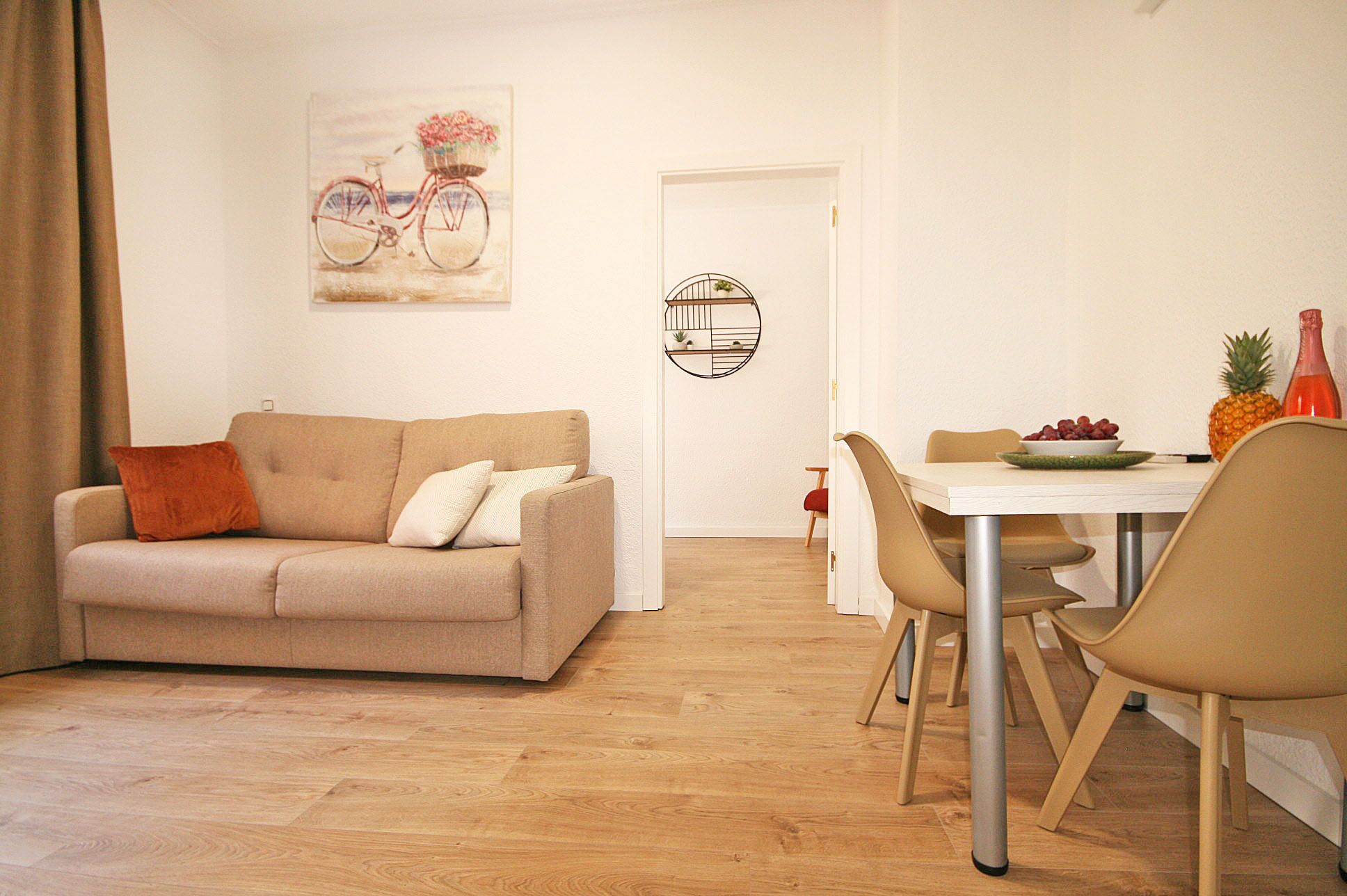 Una sala de estar con un sofá color beige, una mesa de comedor con sillas y una lámpara fijada a la pared.