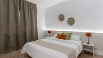 Un dormitorio moderno con una cama grande, dos mesitas de noche con lámparas, un cabecero y un ventanal con cortinas.