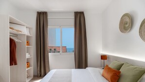 Een hotelkamer met een bed, een kledingkast, een raam met gordijnen en uitzicht op zee.