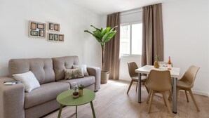 Un salon moderne comprenant un canapé, une table à manger avec des chaises, une petite table verte et une plante en pot.