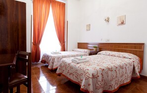 Habitación de hotel con dos camas, cabecera de madera, una mesita de noche con una planta y una silla.